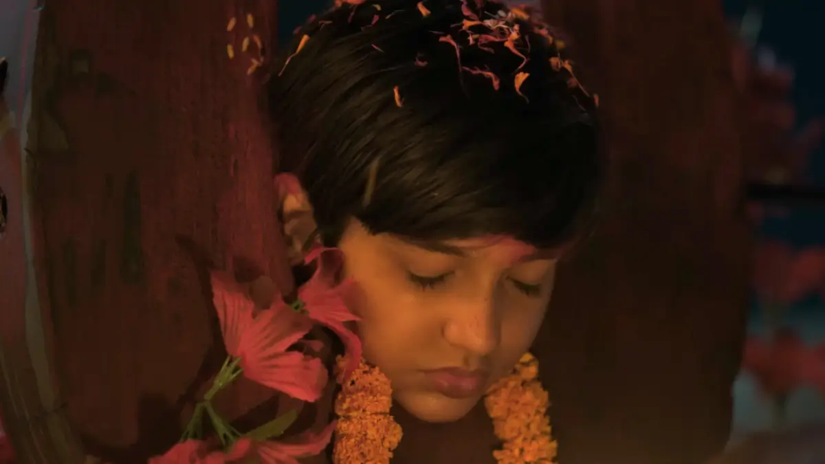 Charak movie scene: Young woman with marigold petals and garlands in hair, eyes closed in prayer, emotional ritual moment