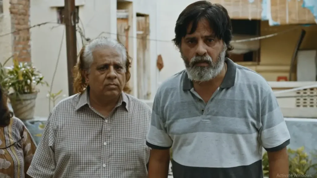 Two older Indian men standing in a narrow alley with serious expressions, one with white hair in checkered shirt, other bearded in grey striped polo