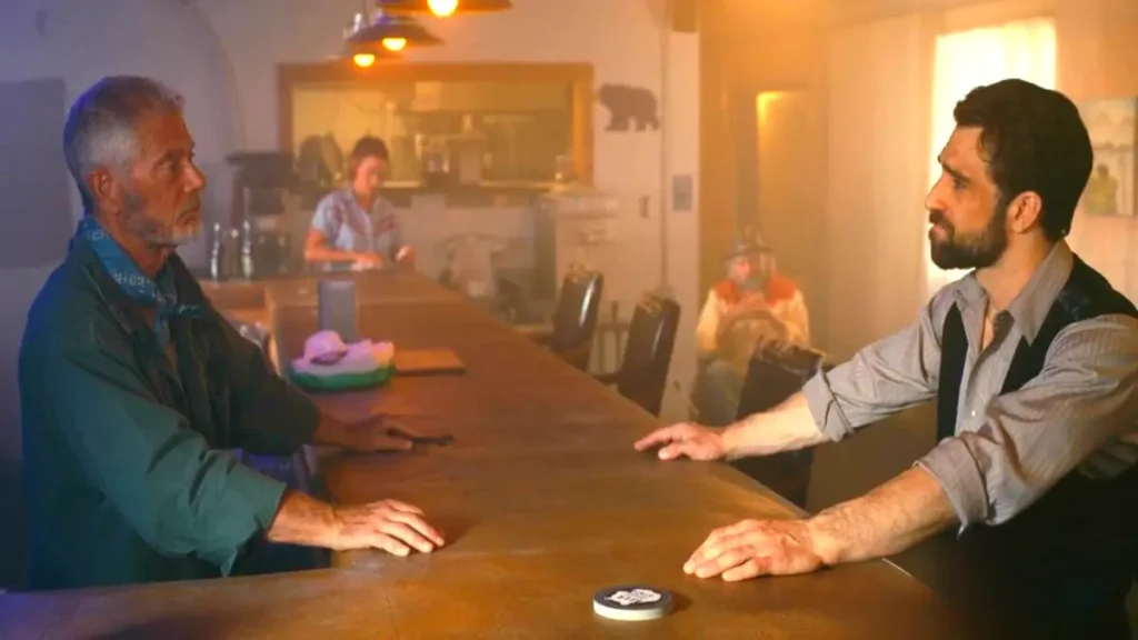 Hellfire 2026 movie scene: Stephen Lang as drifter talking intensely at bar table with younger man, dimly lit rural bar