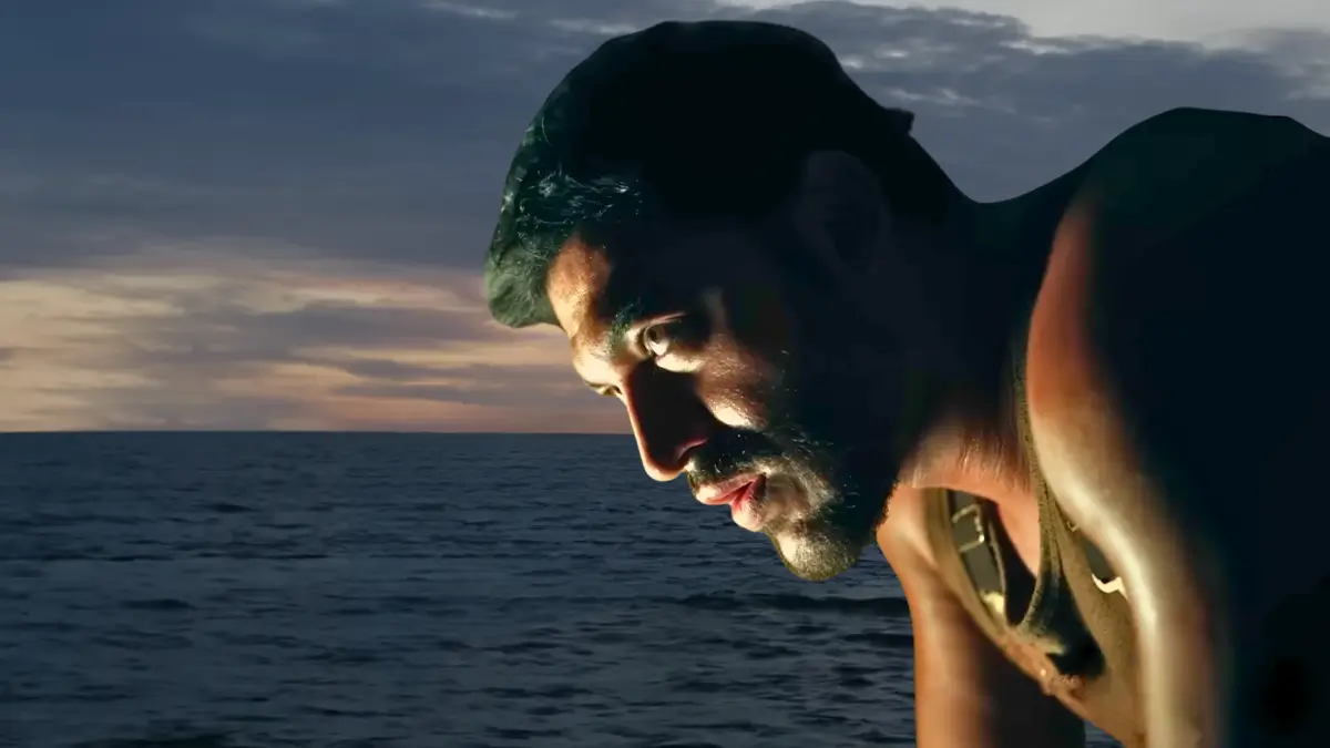 Dead Sea movie scene: Bearded man in tank top leaning over ocean at sunset, intense survival thriller moment on JioHotstar